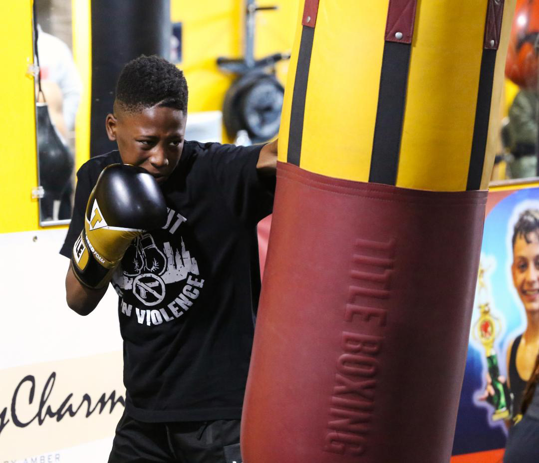 Young boxer training on a heavy bag wearing a Knockout Gun Violence shirt
